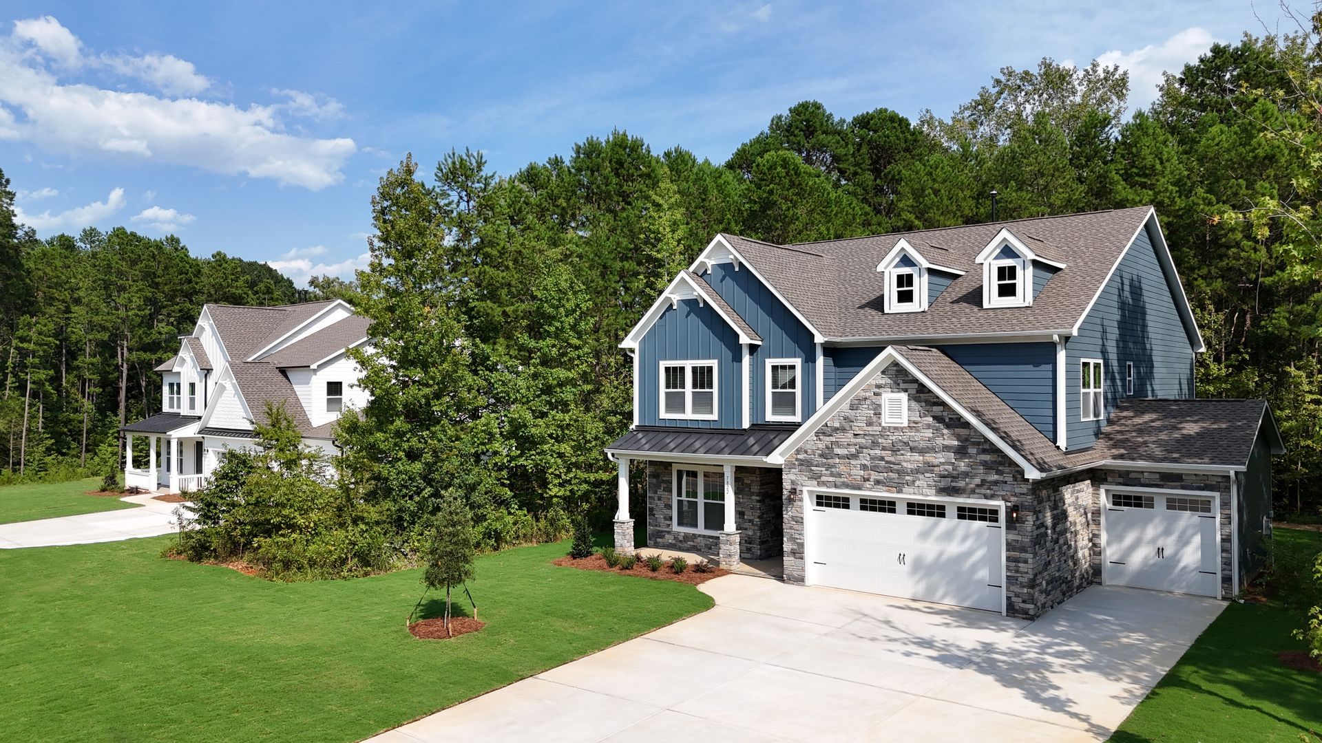 Two-story houses with blue siding and stone accents, set in a green, wooded area.