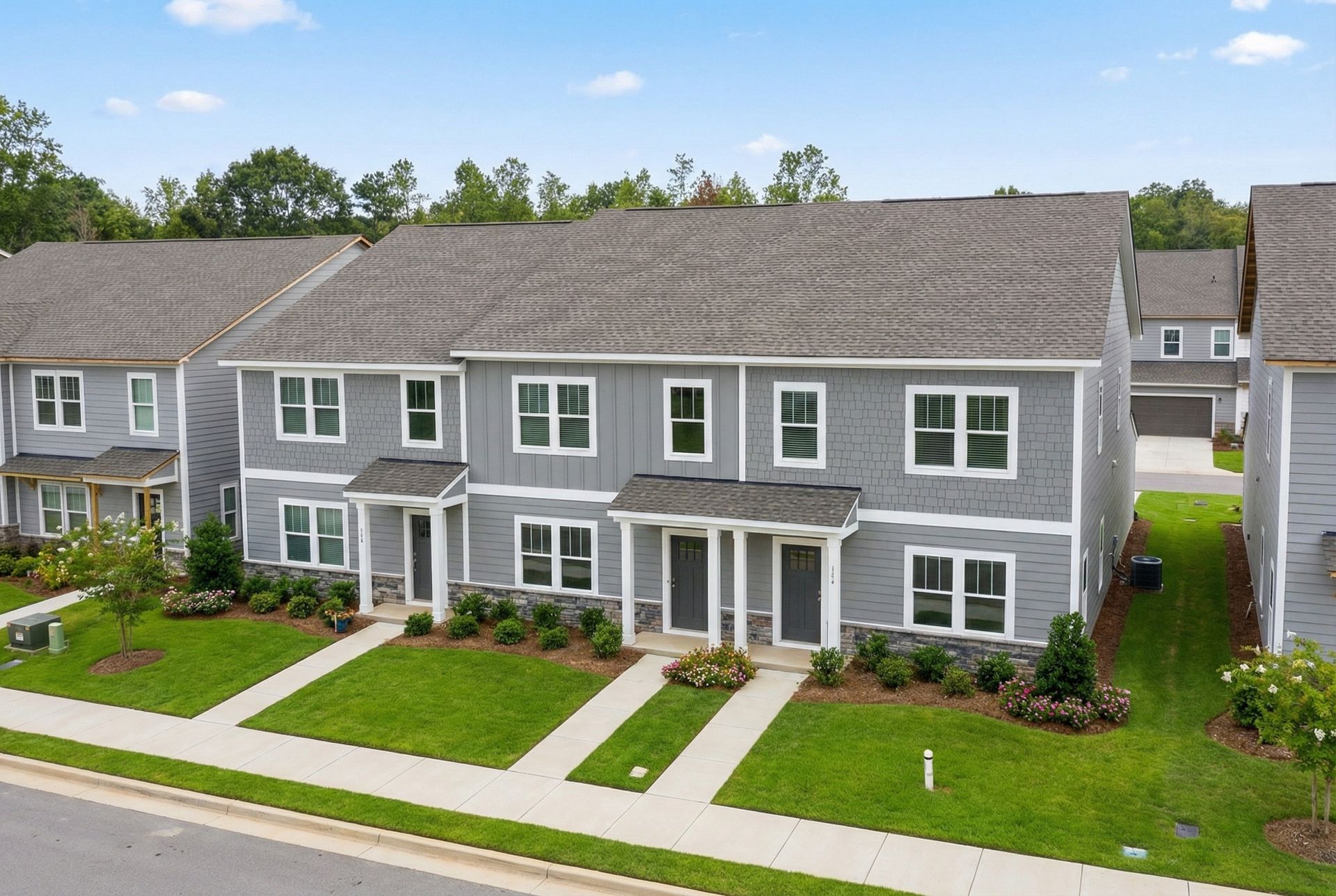 Row of gray townhouses with white trim and green lawns under a clear blue sky