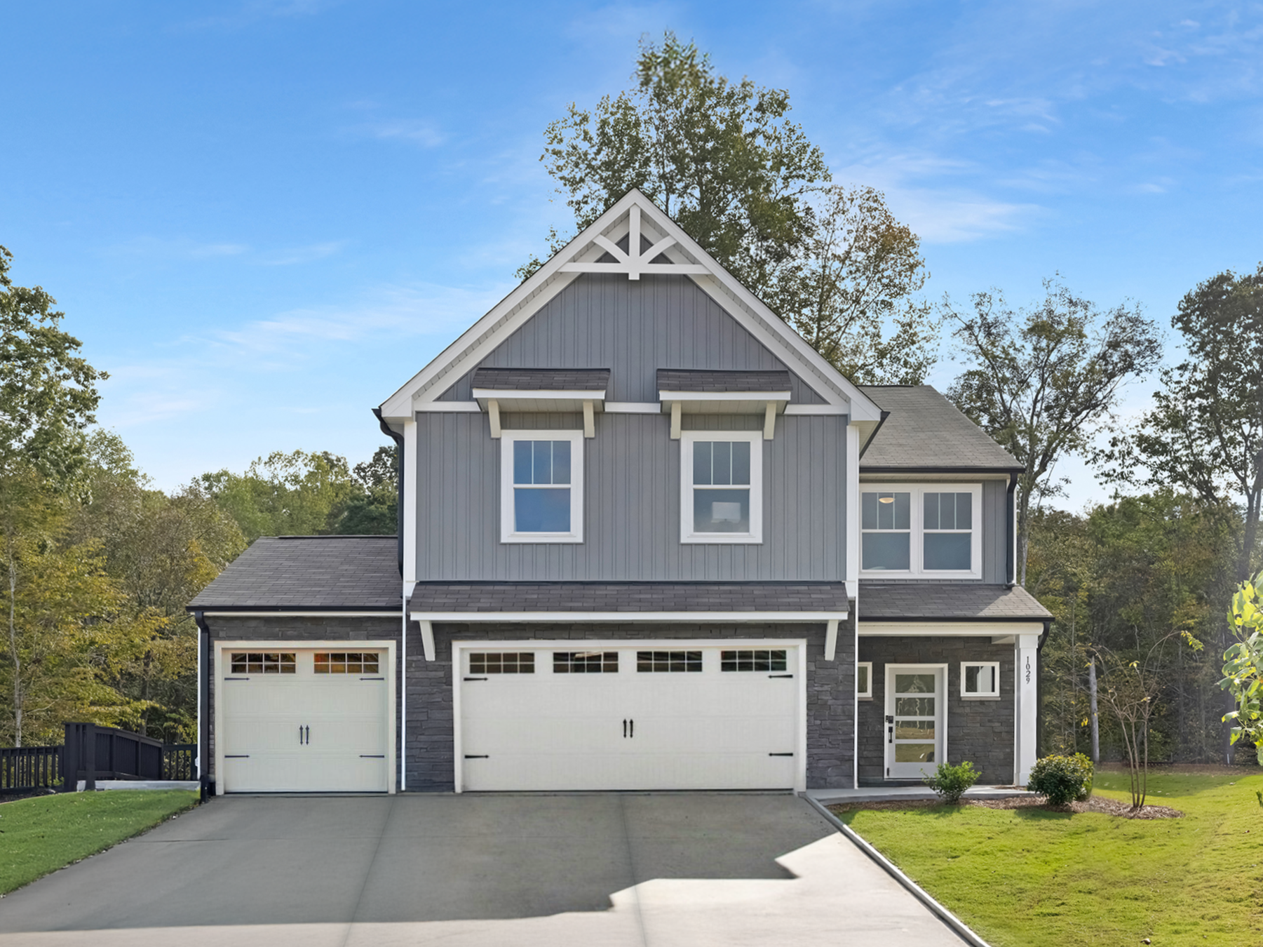 Gray two-story house with three-car garage and driveway under a blue sky