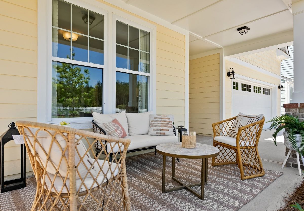 Porch with wicker furniture, rug, and coffee table in front of a house with yellow siding.