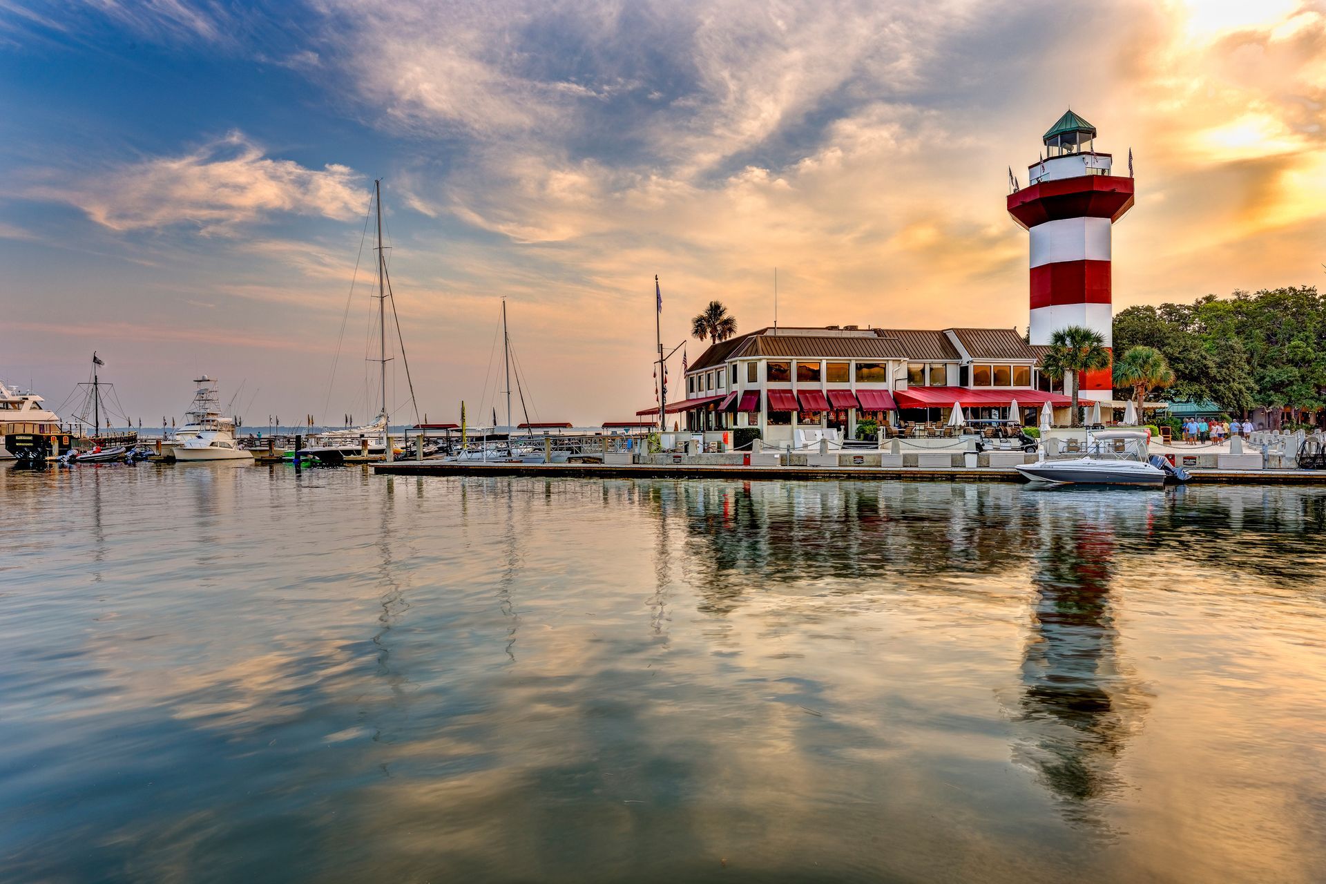 Harbour Town Lighthouse and marina at sunset. Red and white lighthouse reflects in calm water.