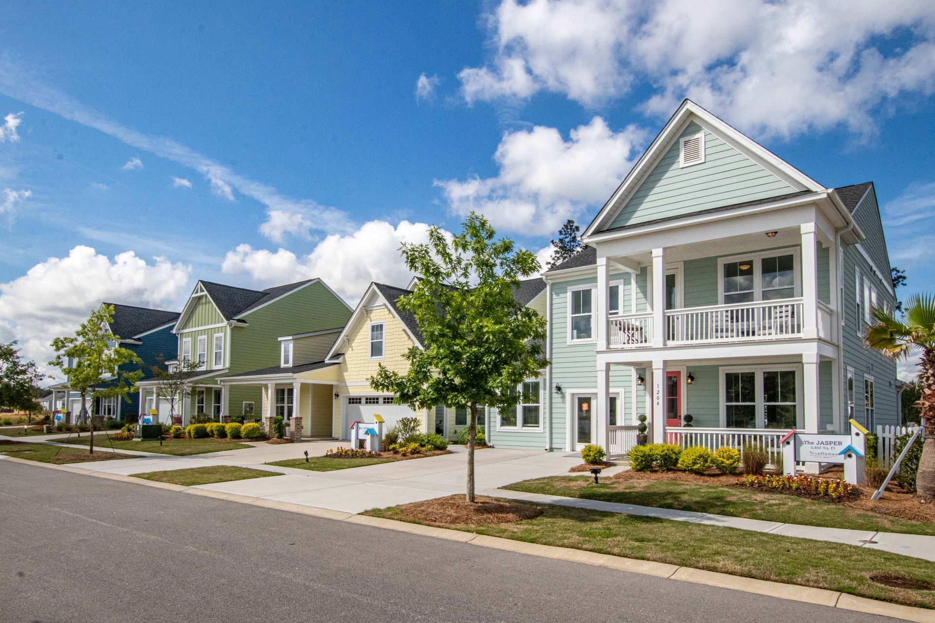 Row of modern suburban houses with porches and small trees under a partly cloudy sky