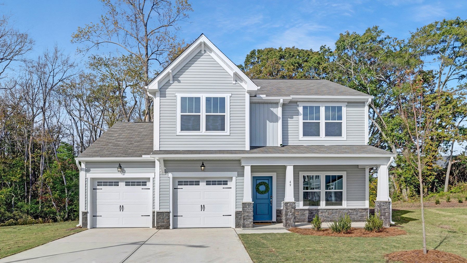 Two-story house with gray siding and white trim, blue door, two-car garage, and trees in the background.