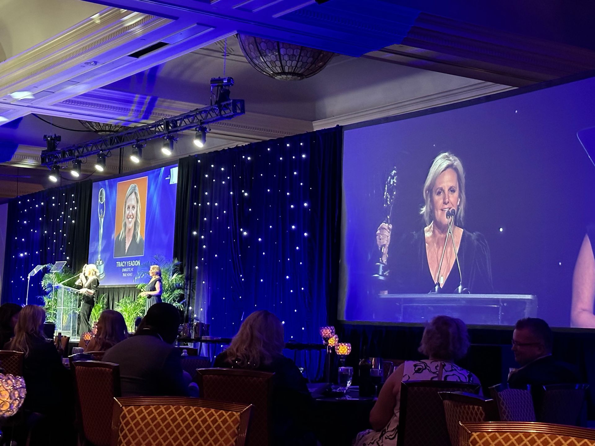 A woman is giving a speech at a conference in front of a large screen.