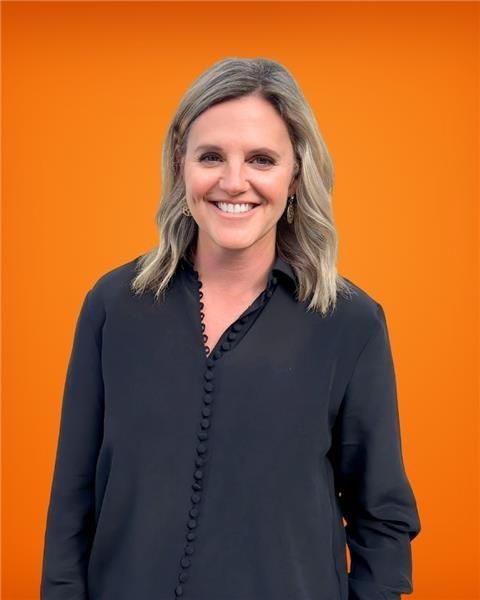 A woman in a black shirt is smiling in front of an orange background