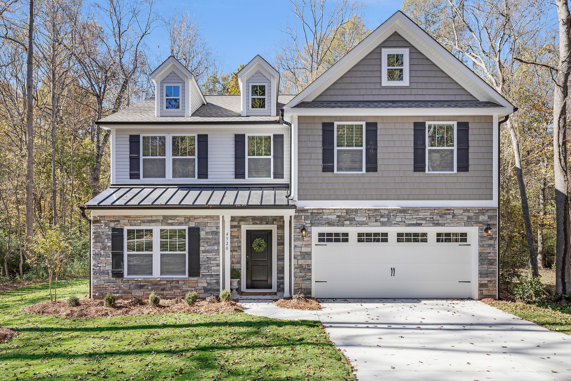 Two-story house with stone, gray siding, and white trim. Garage, shutters, dormers, and a paved driveway.