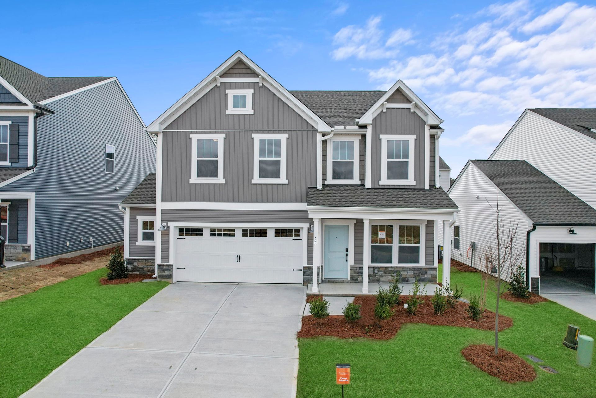 Two-story gray house with white trim, front porch, and a two-car garage on a grassy lawn.