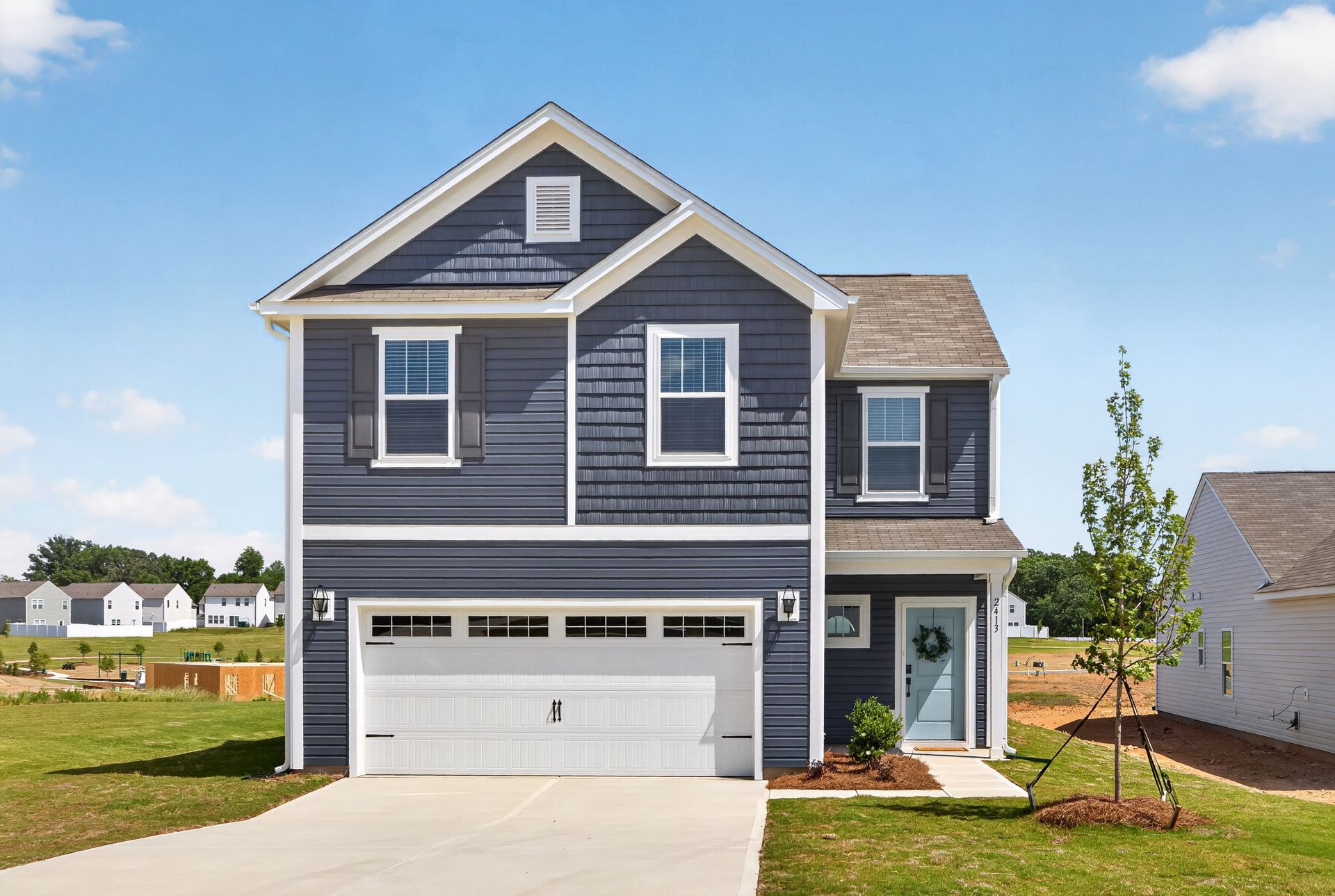 Blue house with white trim, shutters, and walkway, surrounded by green grass and trees.