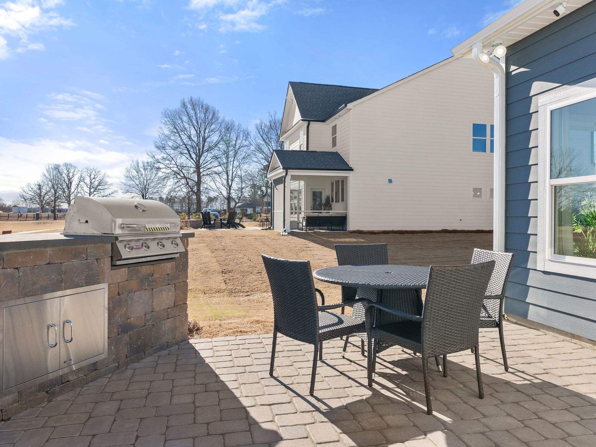 A patio with a table and chairs and a grill in front of a house.