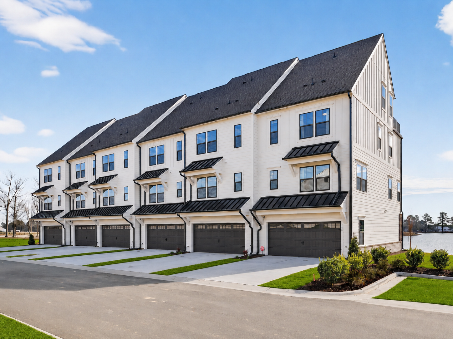 Row of modern townhouses with light brick, white siding, dark roofs, and small front yards.