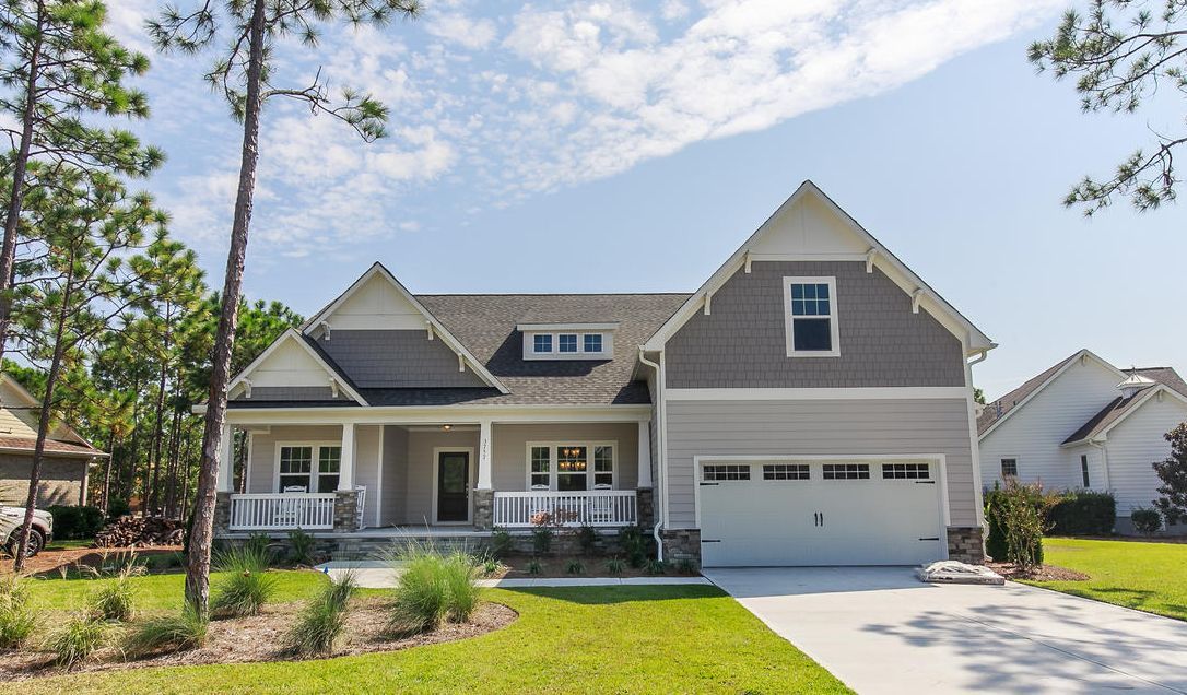 Gray house with porch, garage, and landscaping under a blue sky.