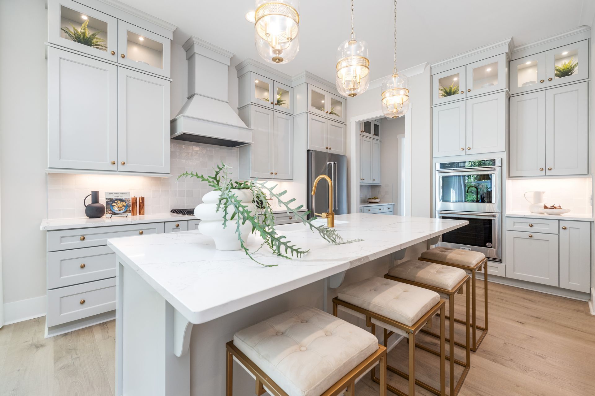 Bright, modern kitchen with white cabinets, island, and gold accents; three pendant lights hang above.