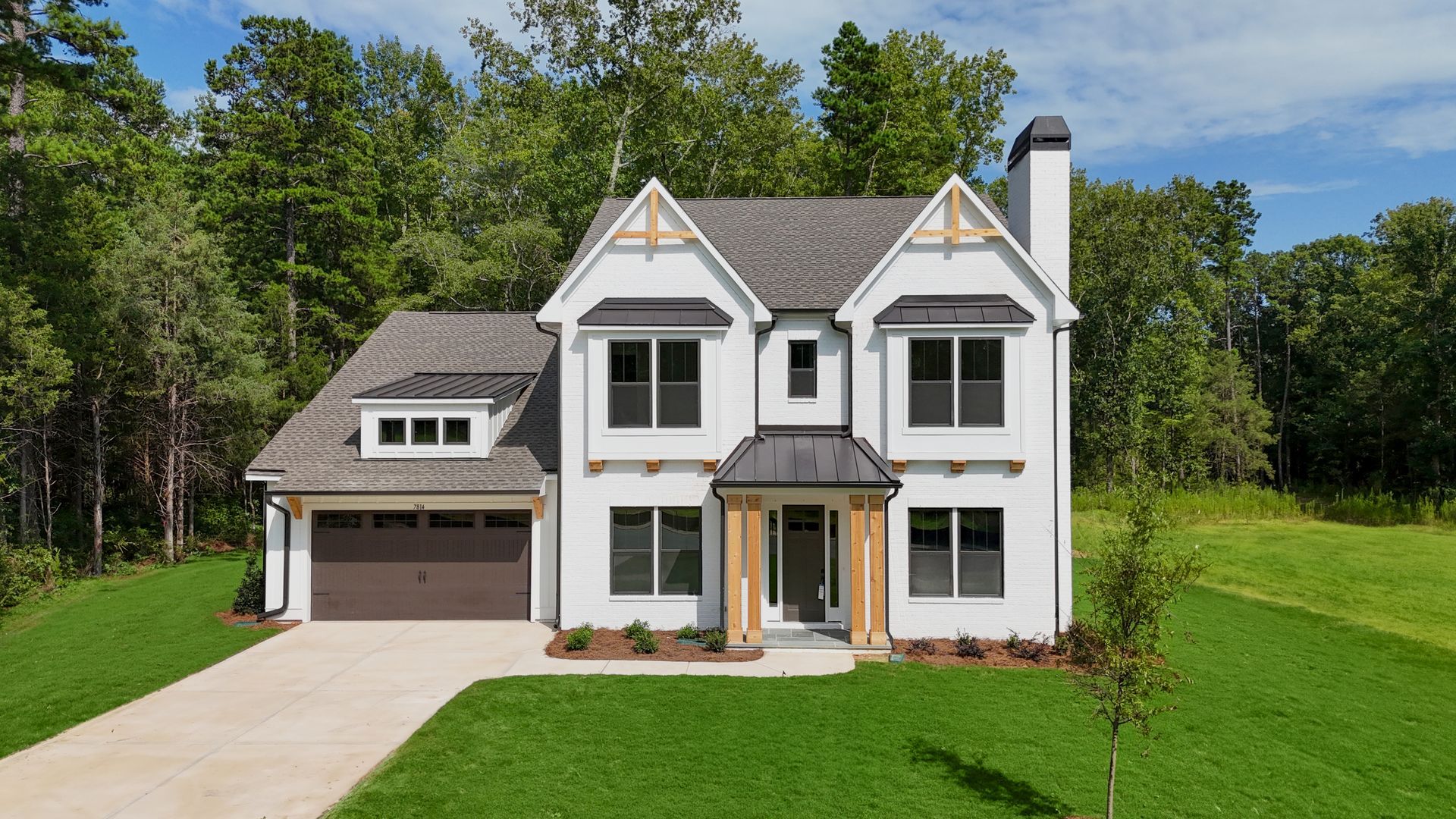 Two-story white house with gray roof, attached garage, and green lawn in a wooded setting.