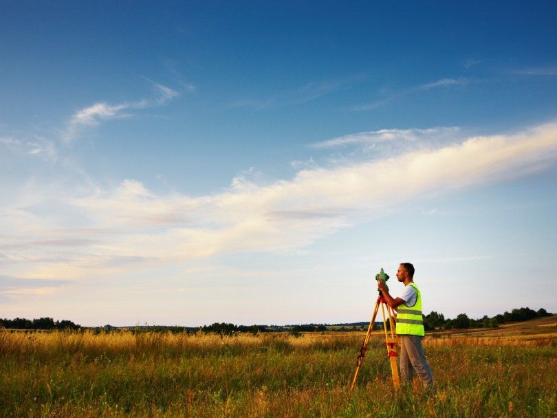 A man is standing in a field using a theodolite.