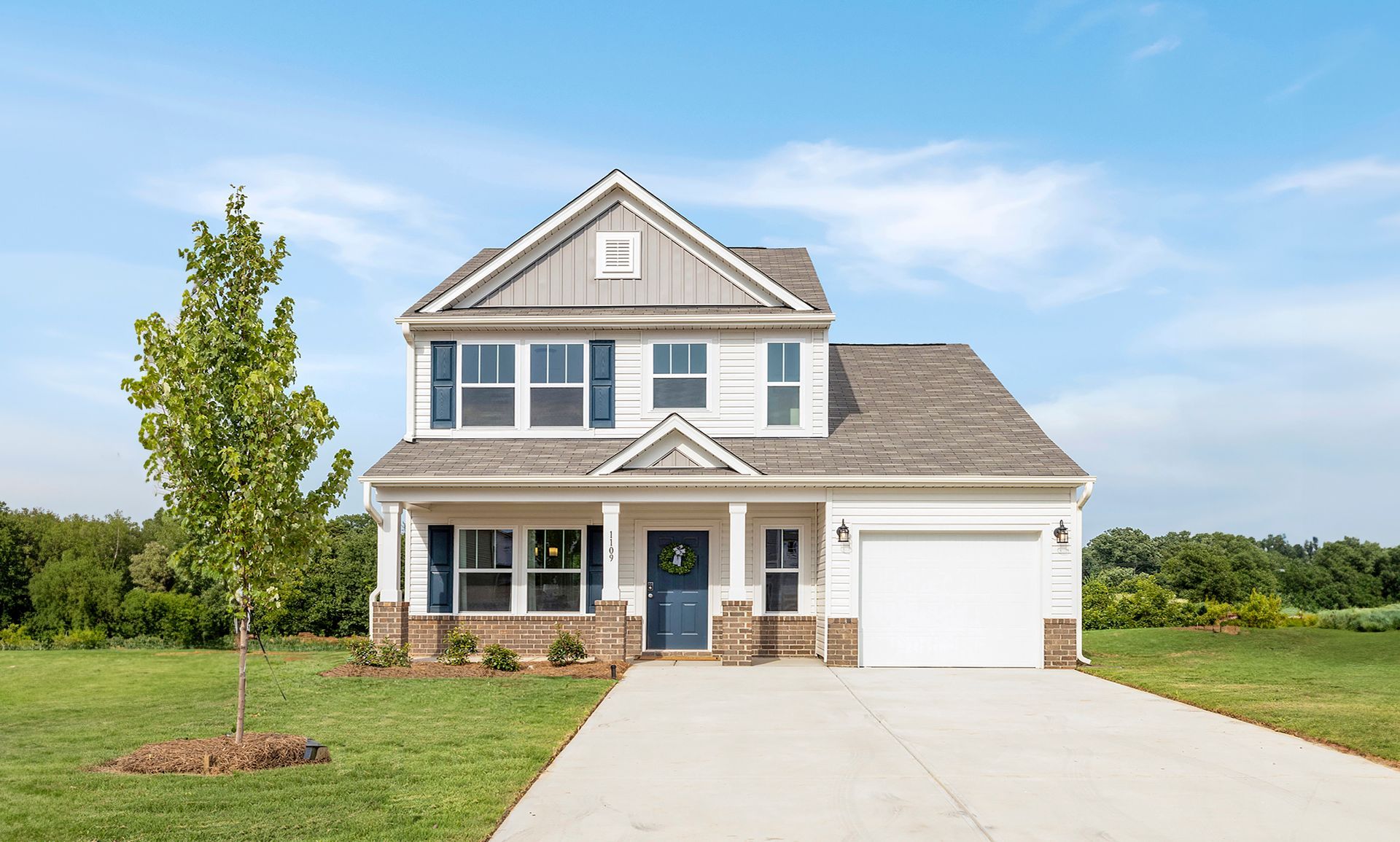 Two-story white house with blue shutters, a blue door, and a gray roof. Green grass and blue sky.