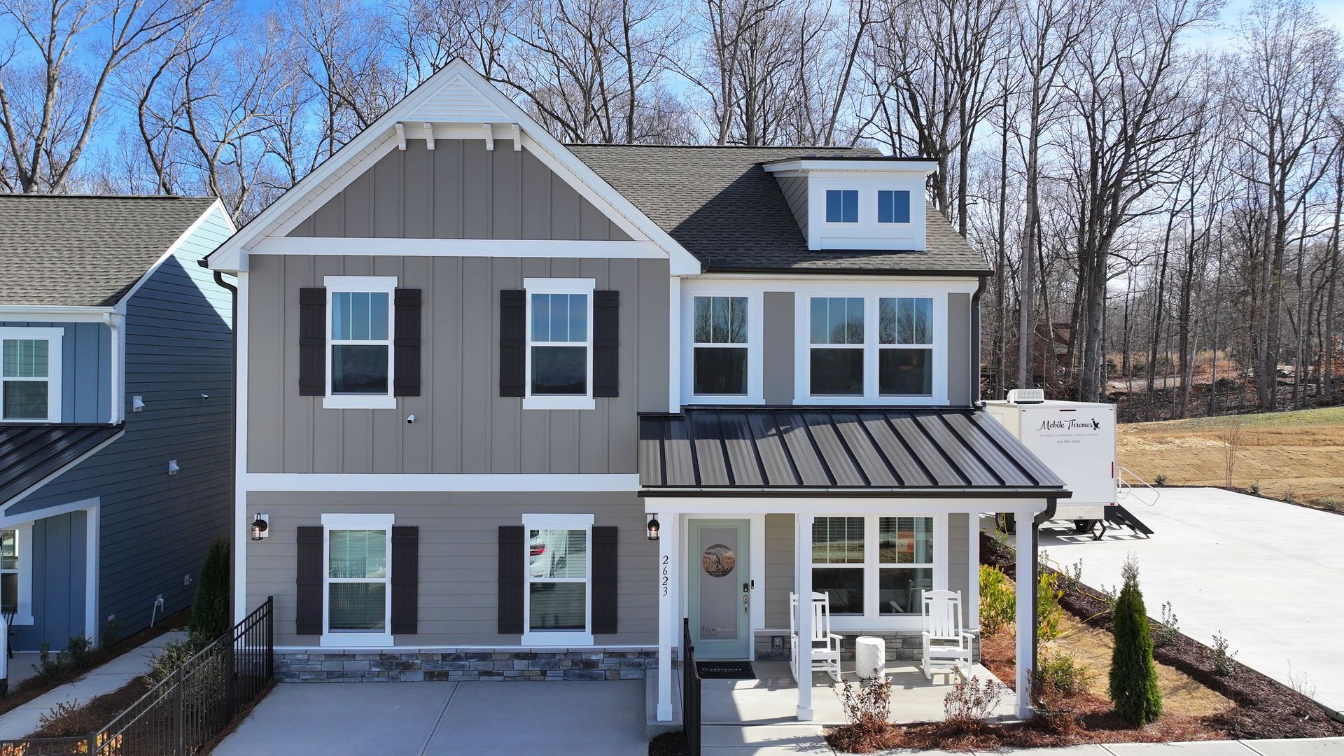 Two-story gray house with black shutters, white trim, and small front porch; blue sky and trees in the background.