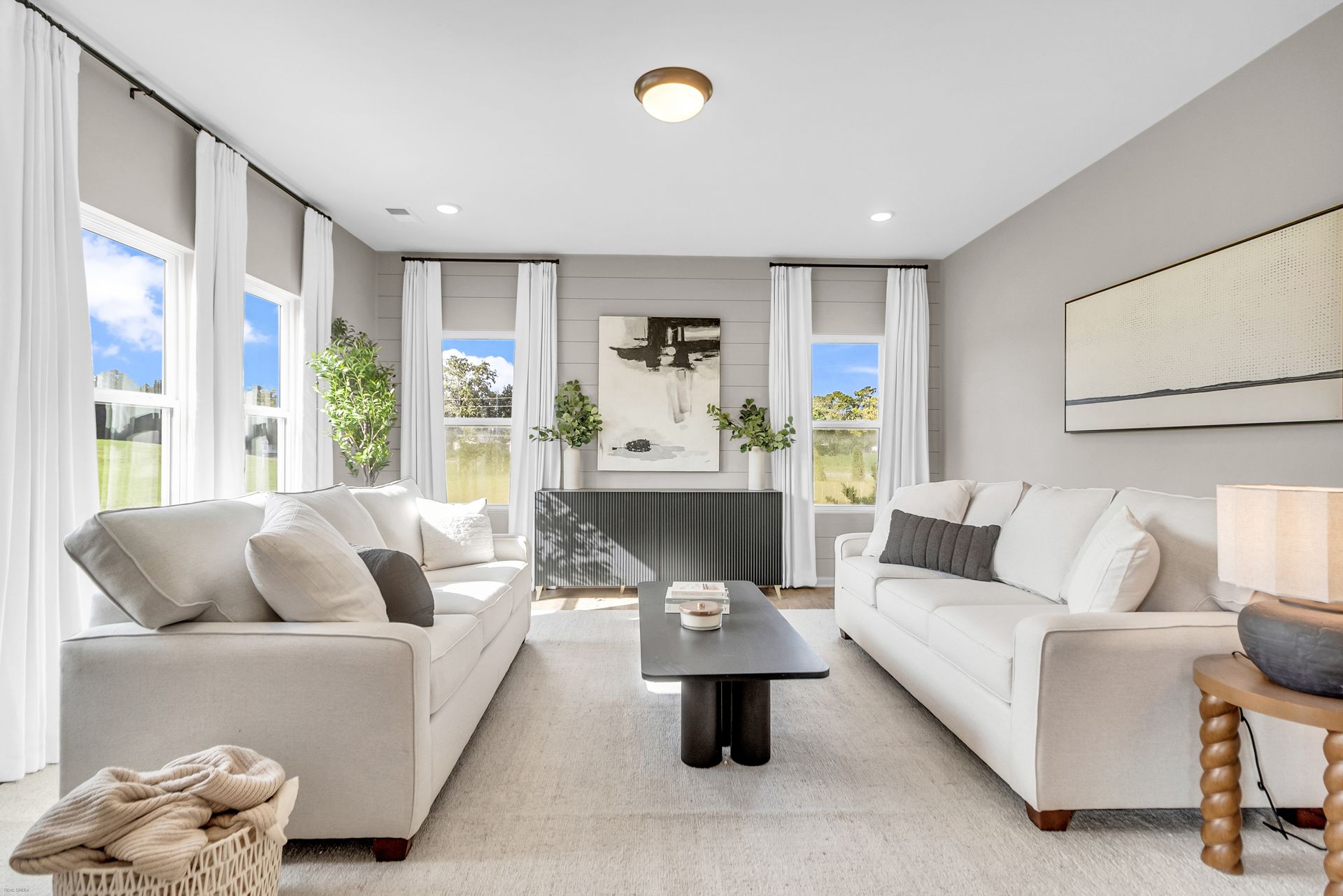 Bright modern living room with white sofas, large windows, and a dark coffee table
