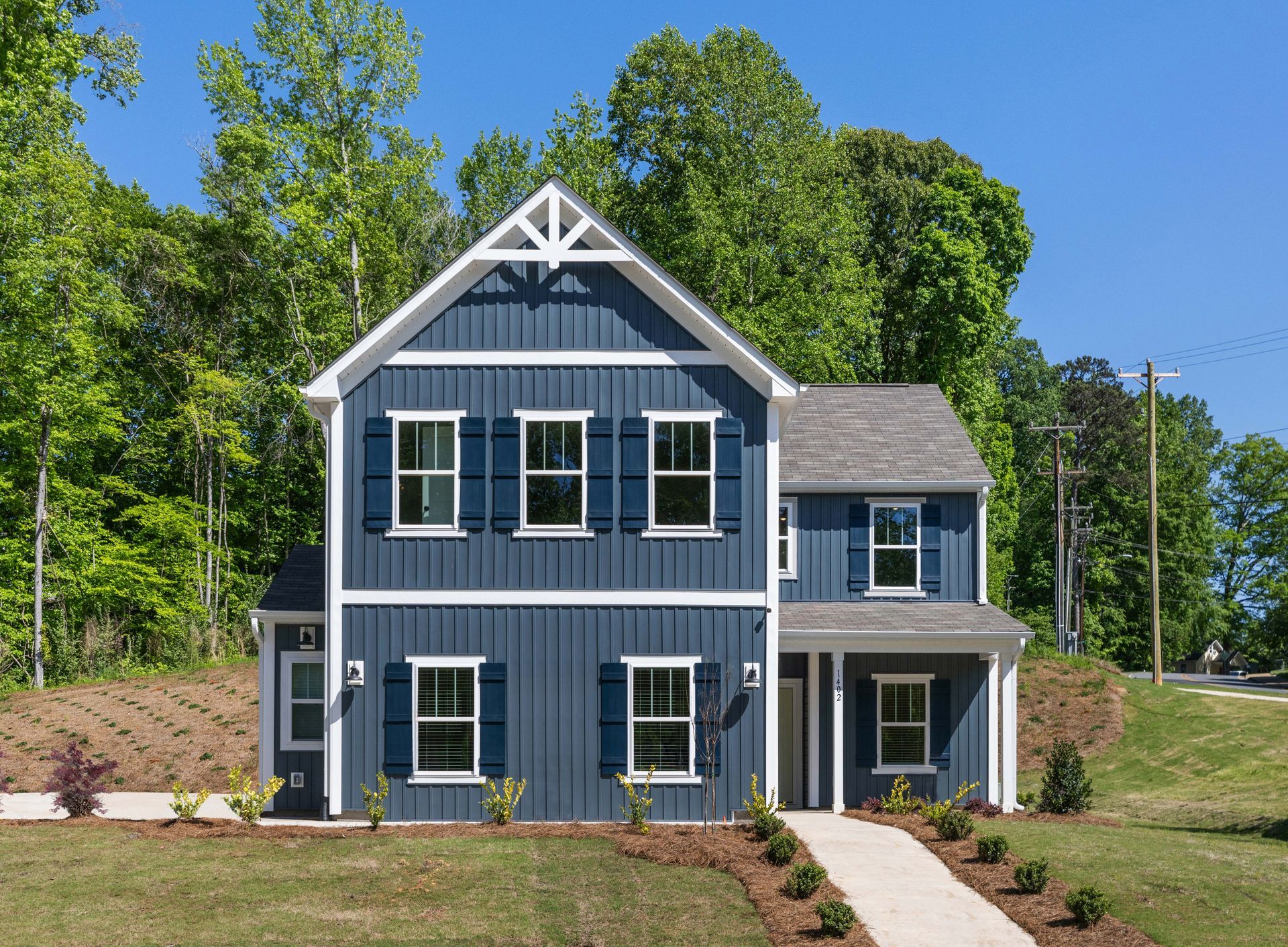 Blue house with white trim, shutters, and walkway, surrounded by green grass and trees.