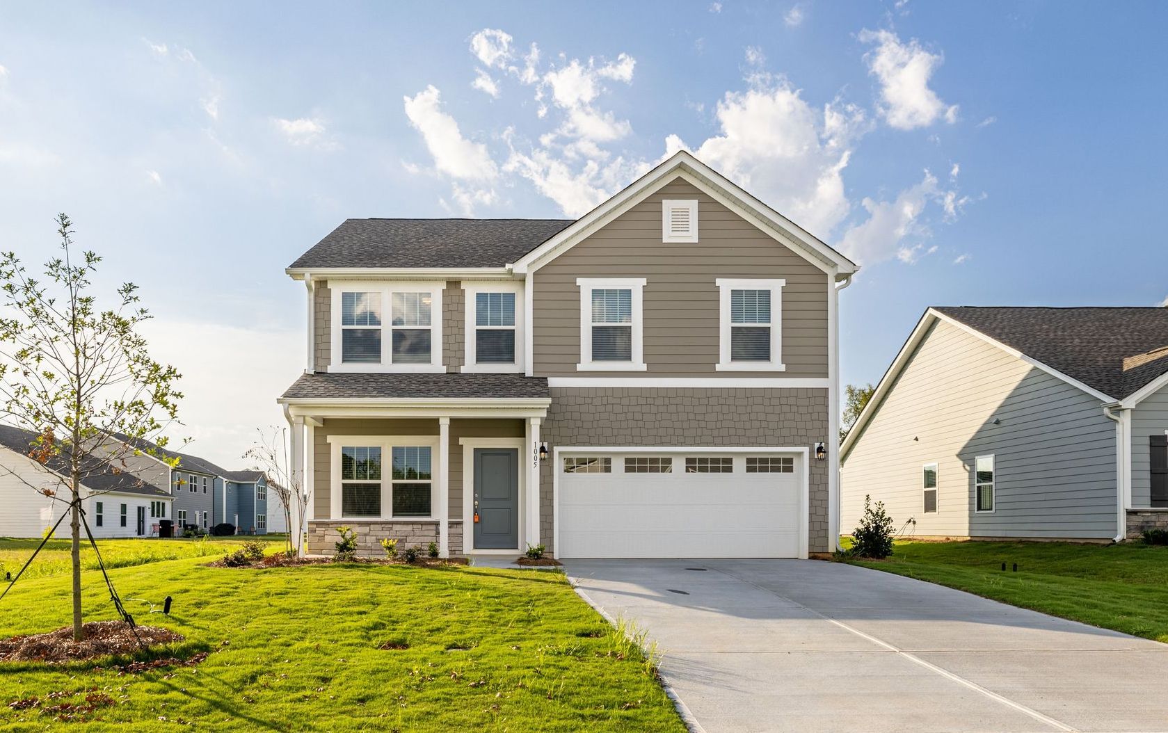 Two-story gray house with white garage door and a concrete driveway on a sunny day.
