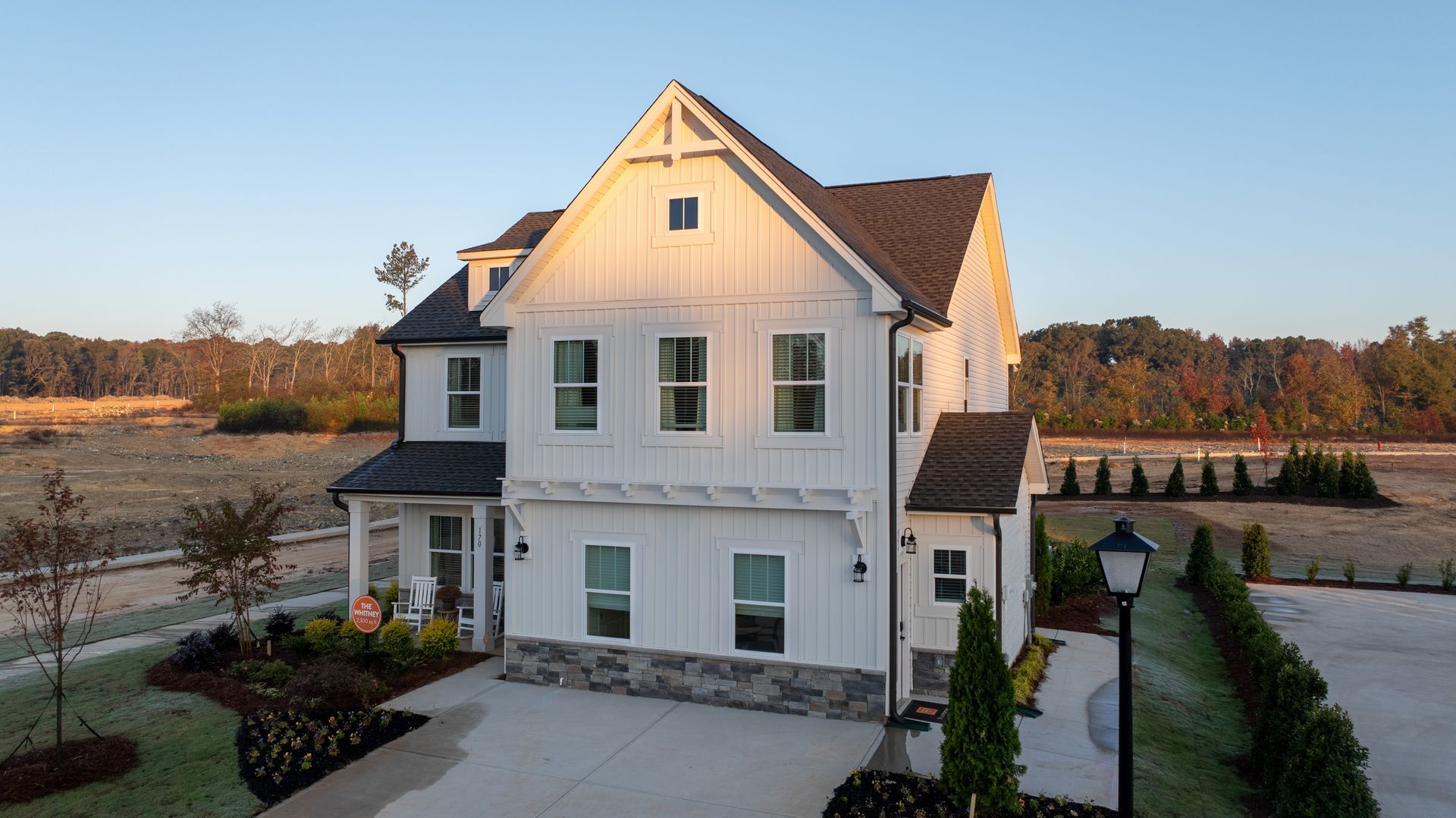 White farmhouse with dark roof, stone base, and manicured landscaping in an open field.