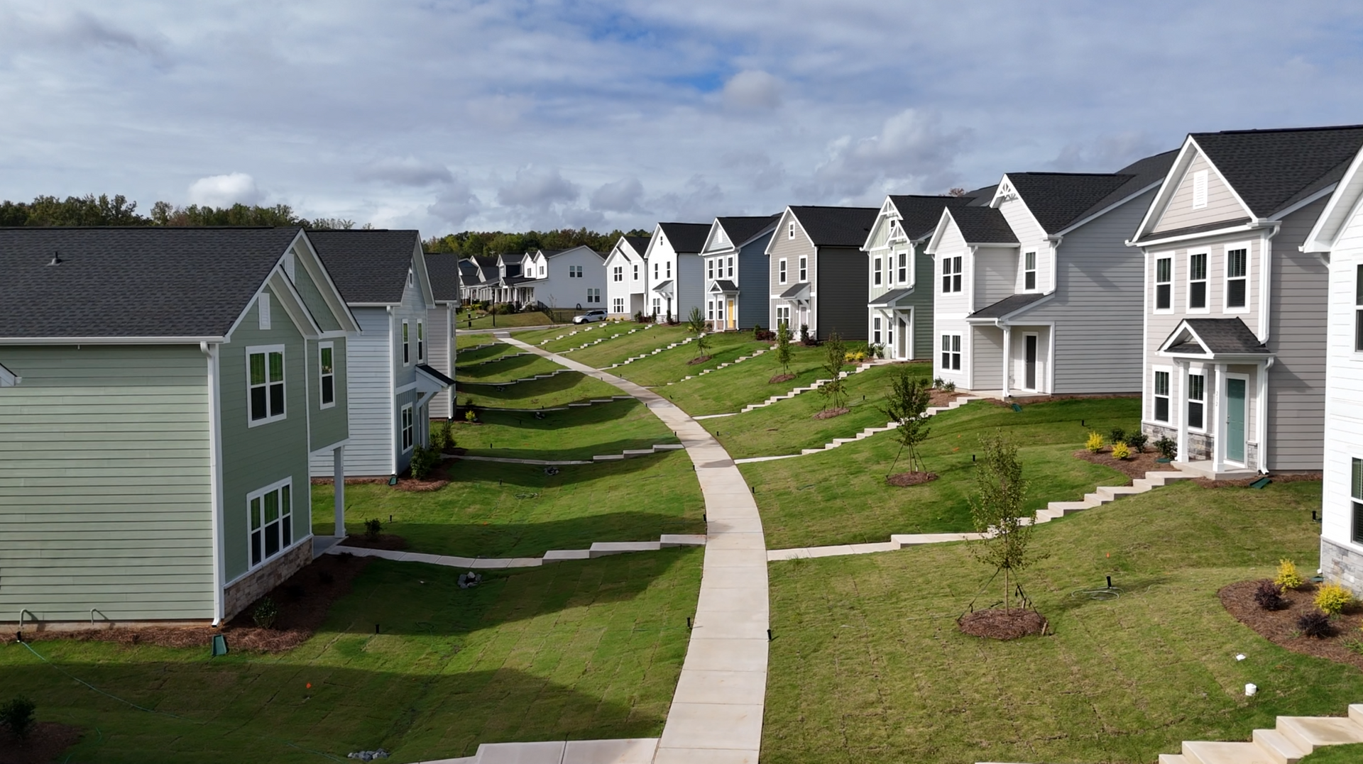 Row of white houses along a curving sidewalk in a green residential neighborhood under a cloudy sky
