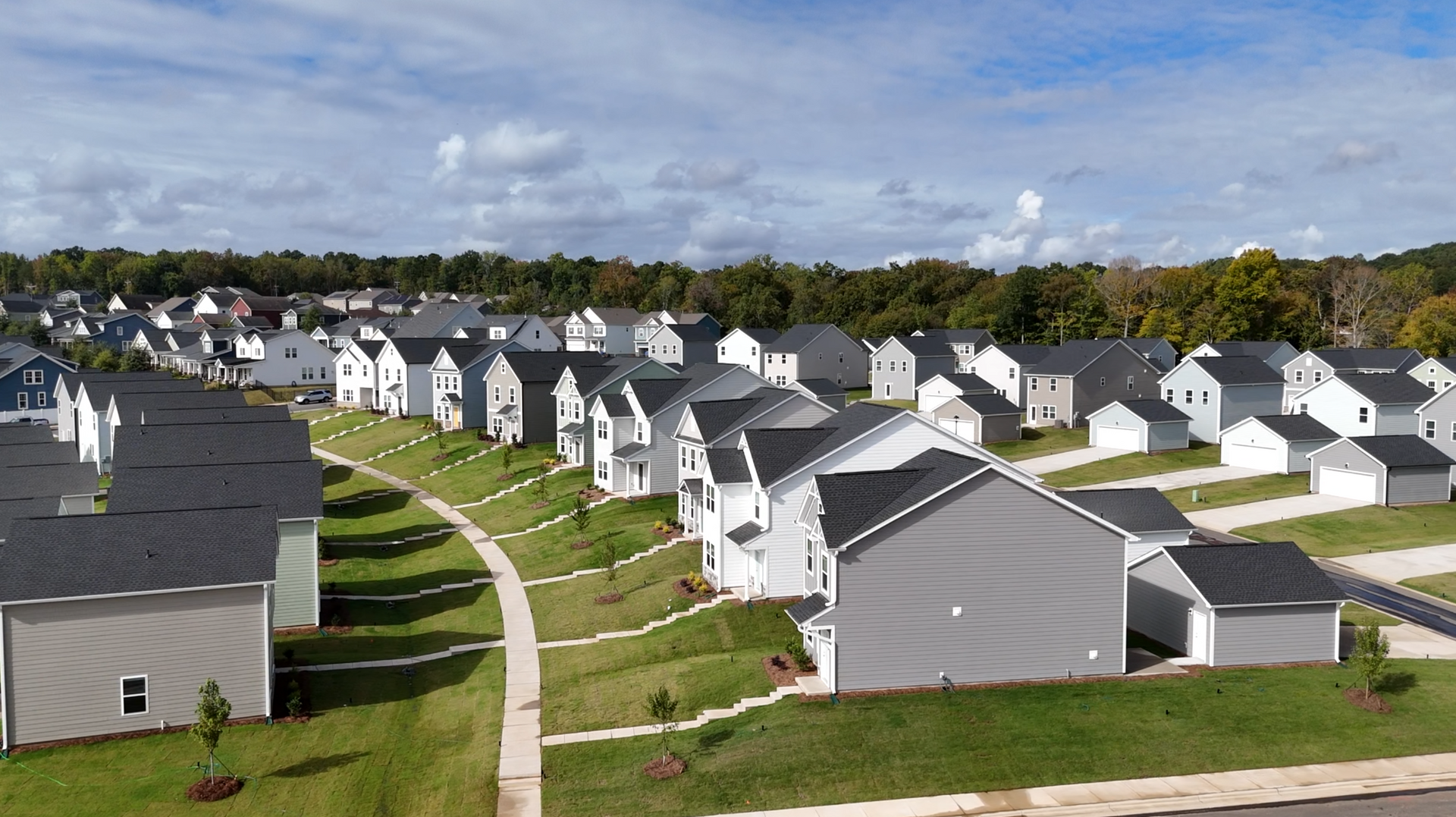 Suburban neighborhood with rows of gray houses, curved streets, and green lawns under a partly cloudy sky