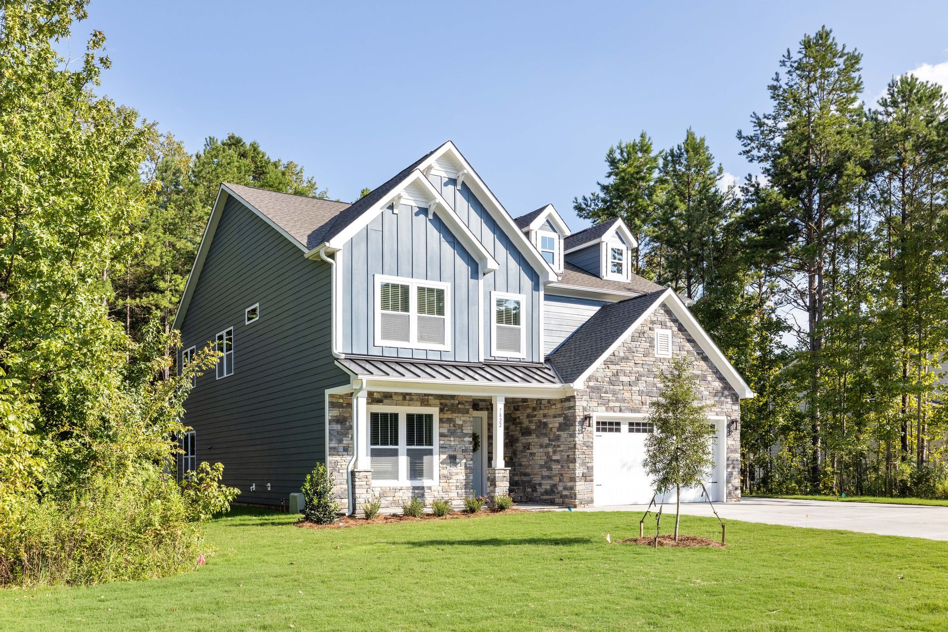Two-story house with blue siding, stone facade, and a green lawn on a sunny day.