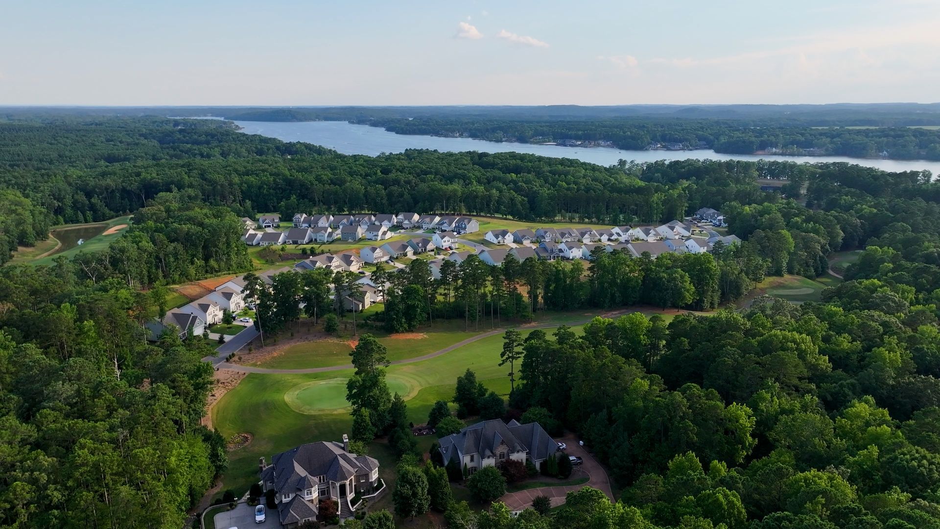 Aerial view: a residential neighborhood near a lake, surrounded by green trees and a golf course.