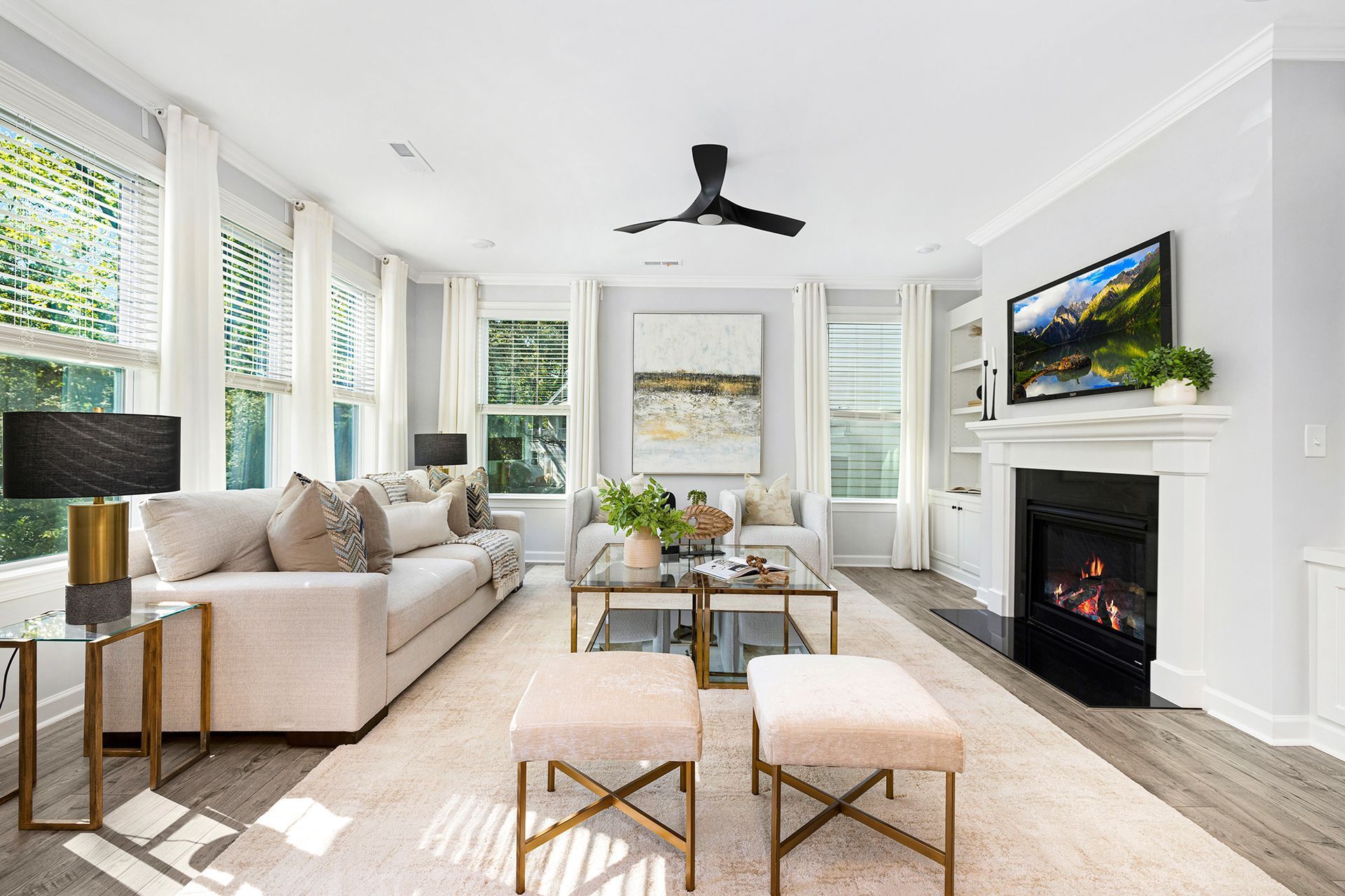 Bright living room with beige sofa, fireplace, wall TV, large windows, and black ceiling fan