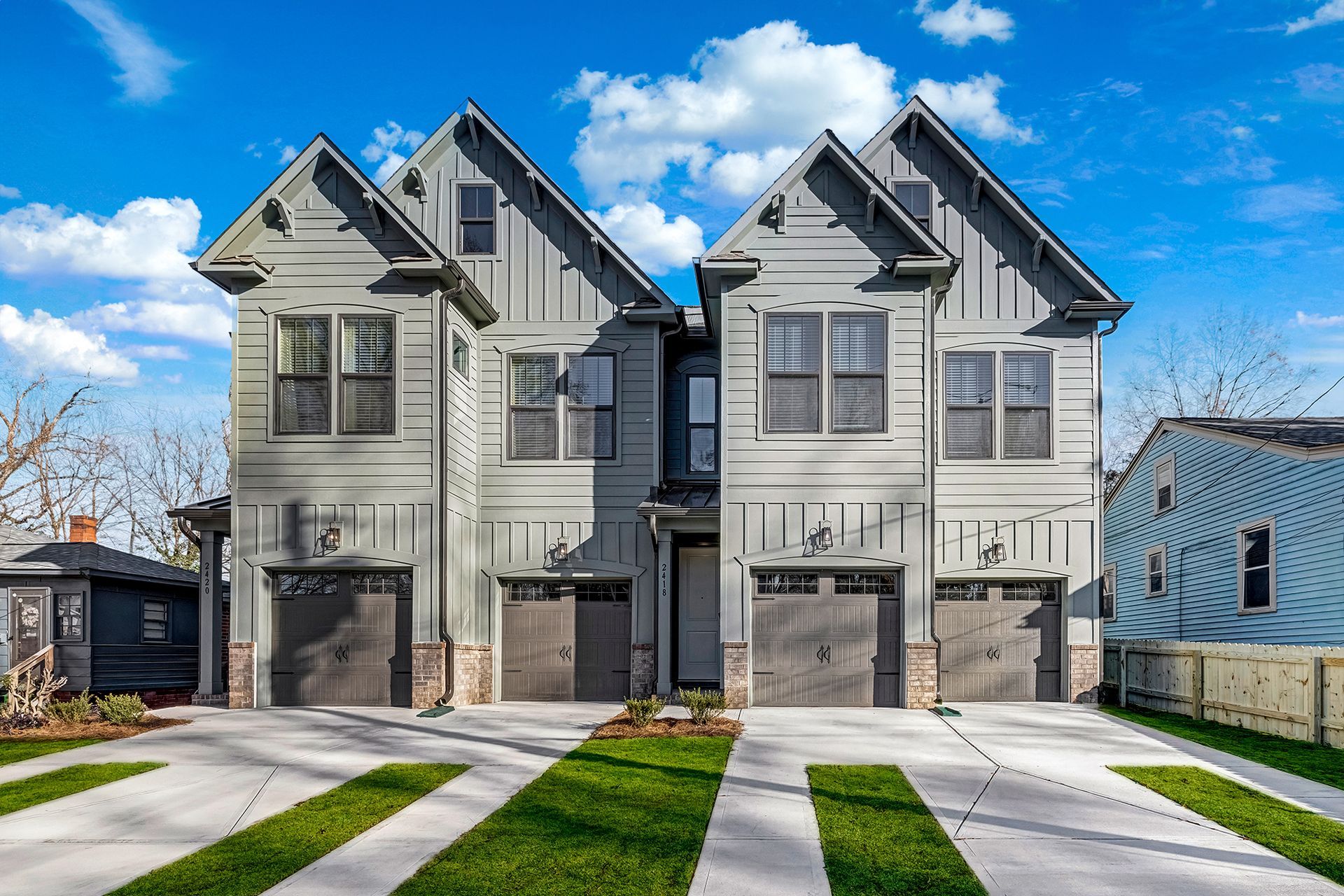 Gray townhouses with gabled roofs and brick accents. Driveways with green grass strips.