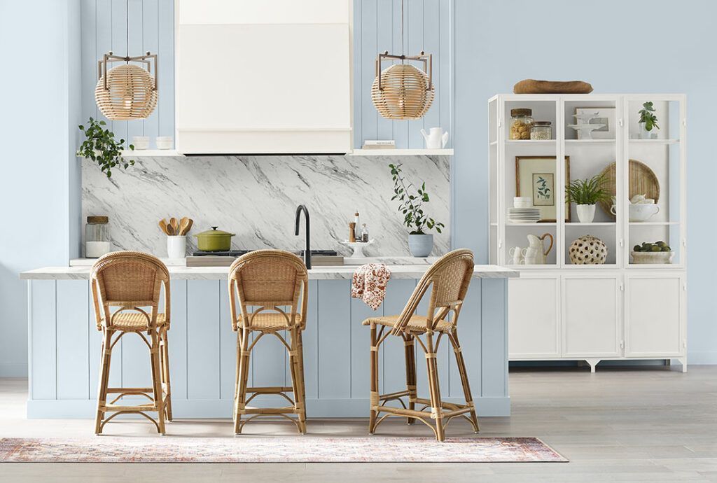 A kitchen with blue walls and white cabinets and wicker chairs.