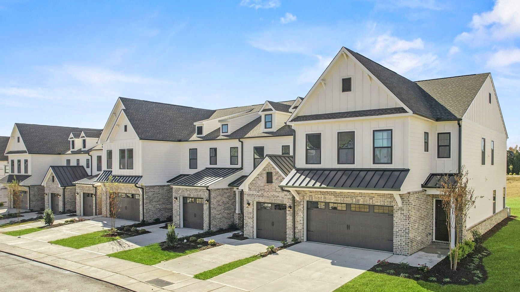 Row of white townhouses with dark roofs and gray garage doors under a blue sky.