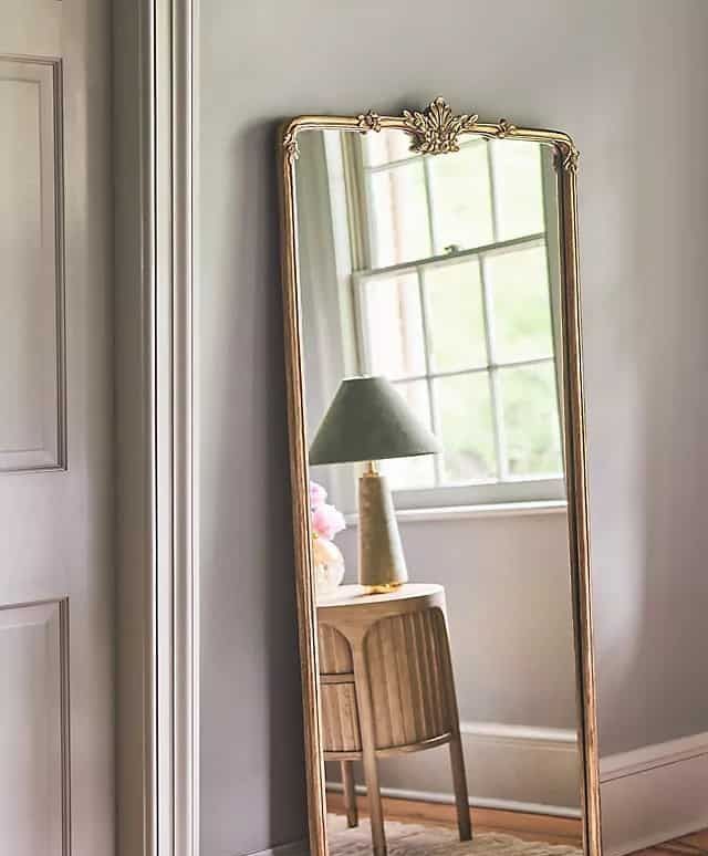 A full length mirror is in a hallway next to a lamp.