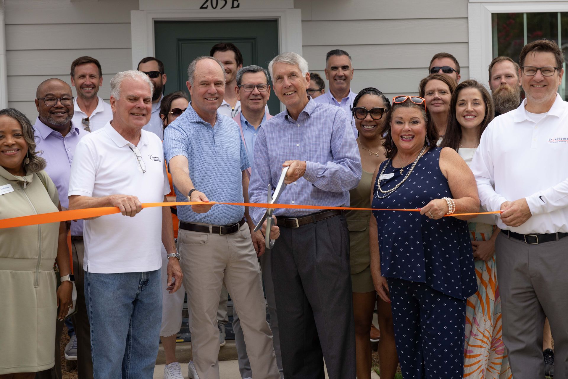 Group cuts orange ribbon in front of a building, celebrating an opening.