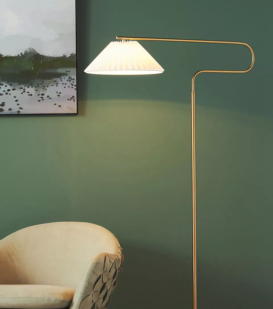 A lamp is sitting next to a chair in front of a green wall.
