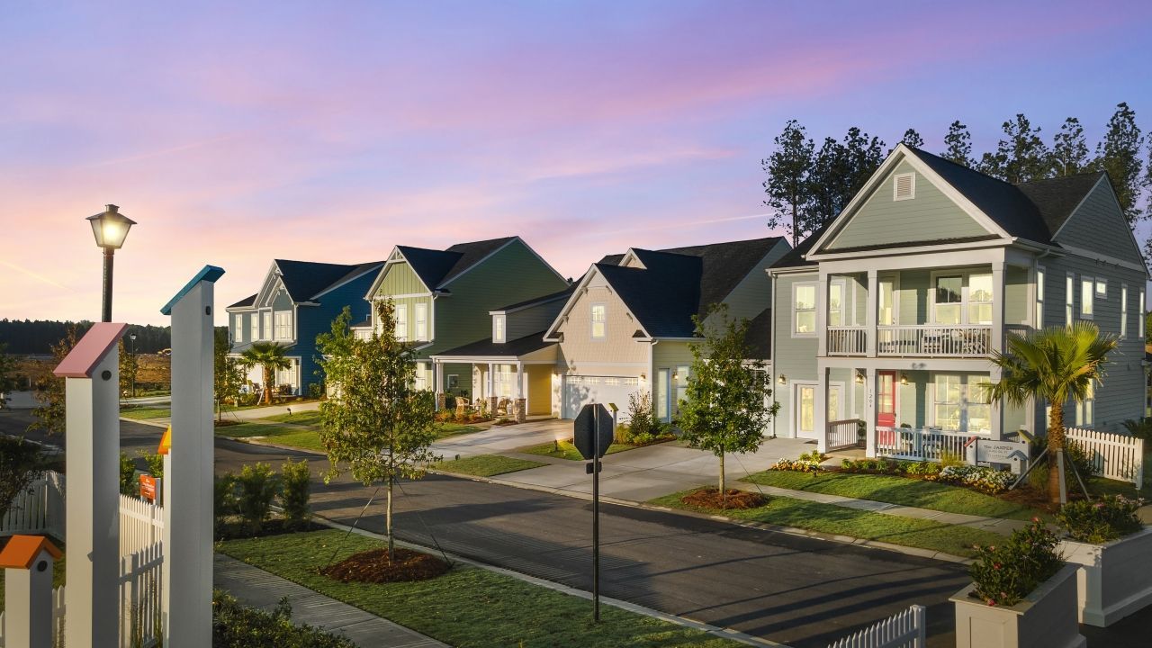 Row of colorful houses along a street at dusk, with a lamppost and picket fence.