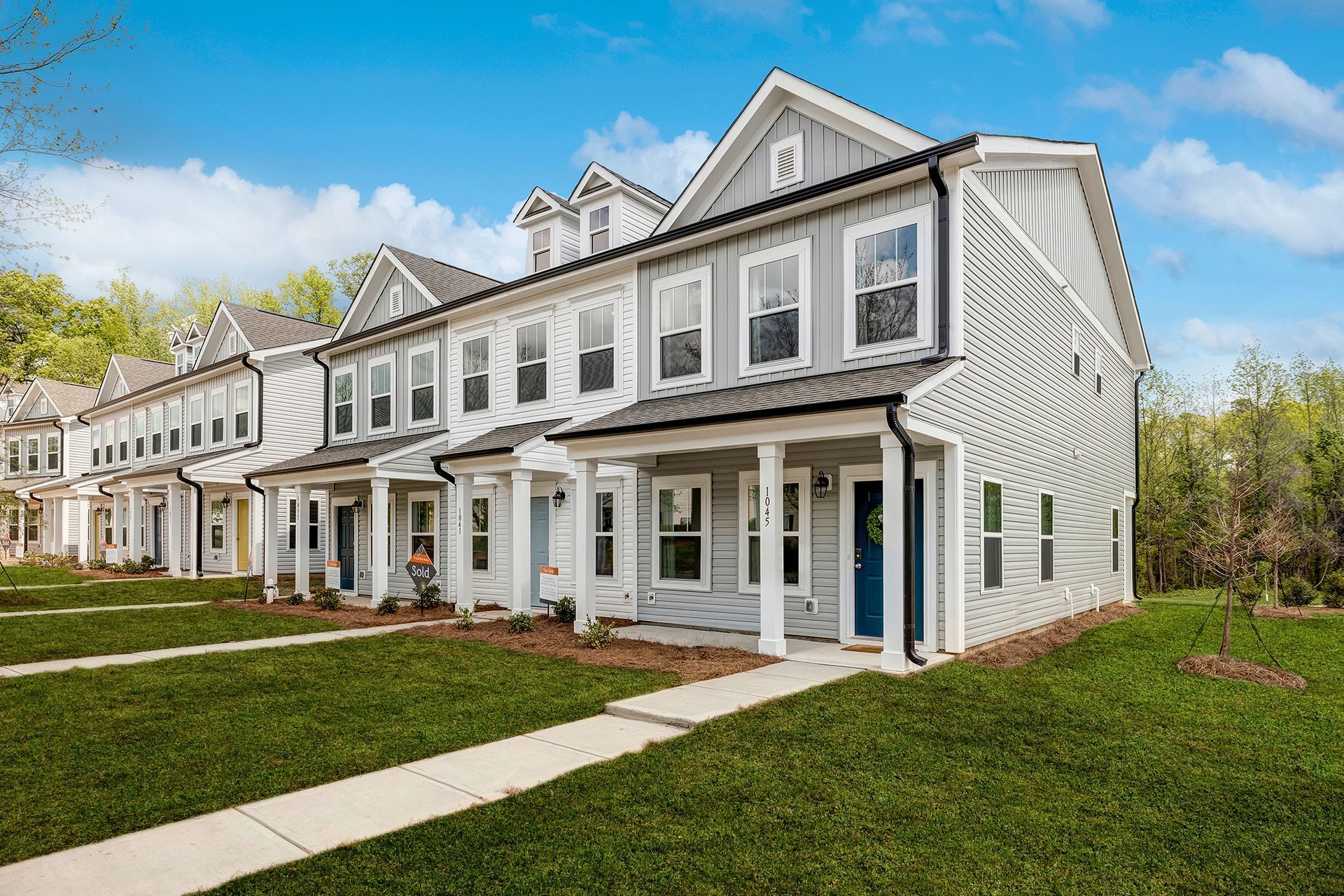 A row of white houses with porches and a sidewalk in front of them.