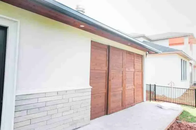 A white house with a wooden garage door and a brick wall.