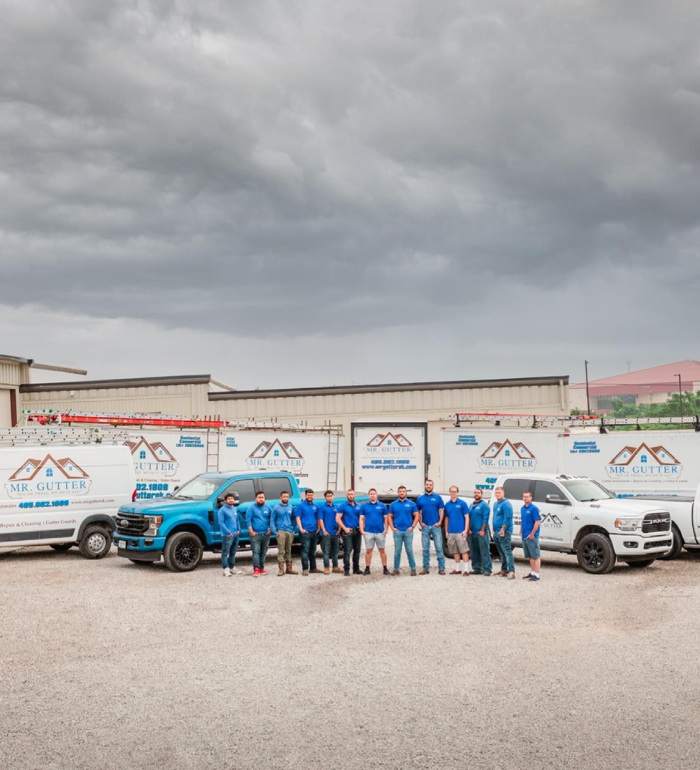 A group of people are posing for a picture in front of a building and trucks.