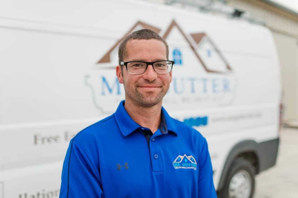 A man wearing glasses and a blue shirt is standing in front of a white van.