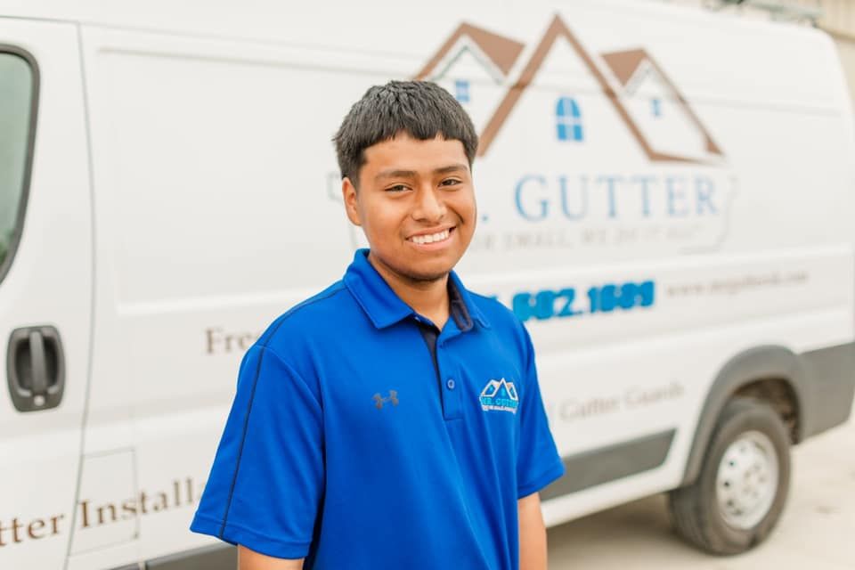 A young man in a blue shirt is standing in front of a white van.