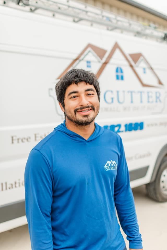 A man in a blue shirt is standing in front of a gutter company van.