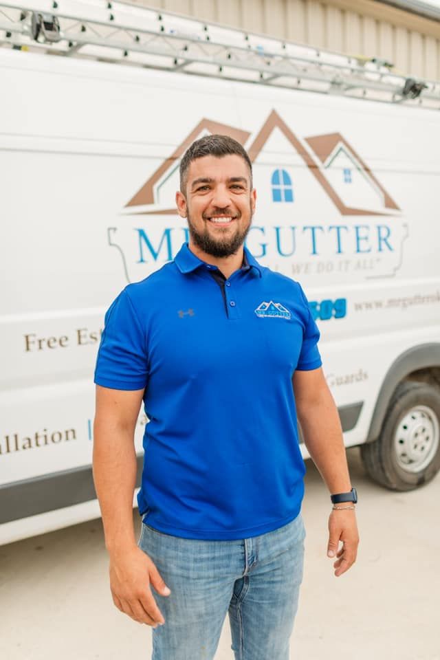 A man in a blue shirt is standing in front of a gutter company van.