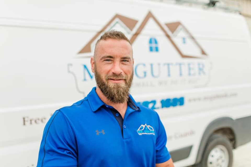 A man in a blue shirt is standing in front of a gutter company van.