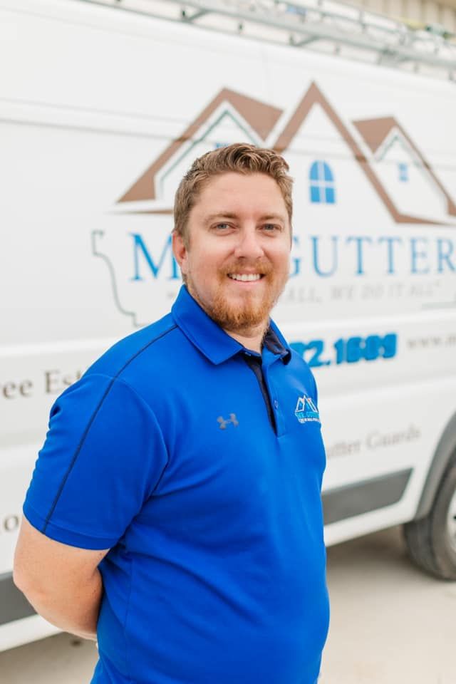 A man in a blue shirt is standing in front of a white van.