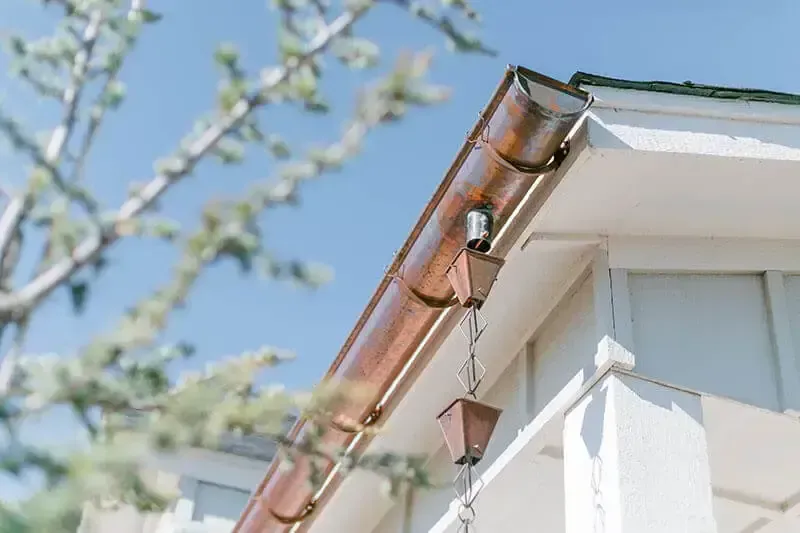 A close up of a copper gutter on the side of a house.