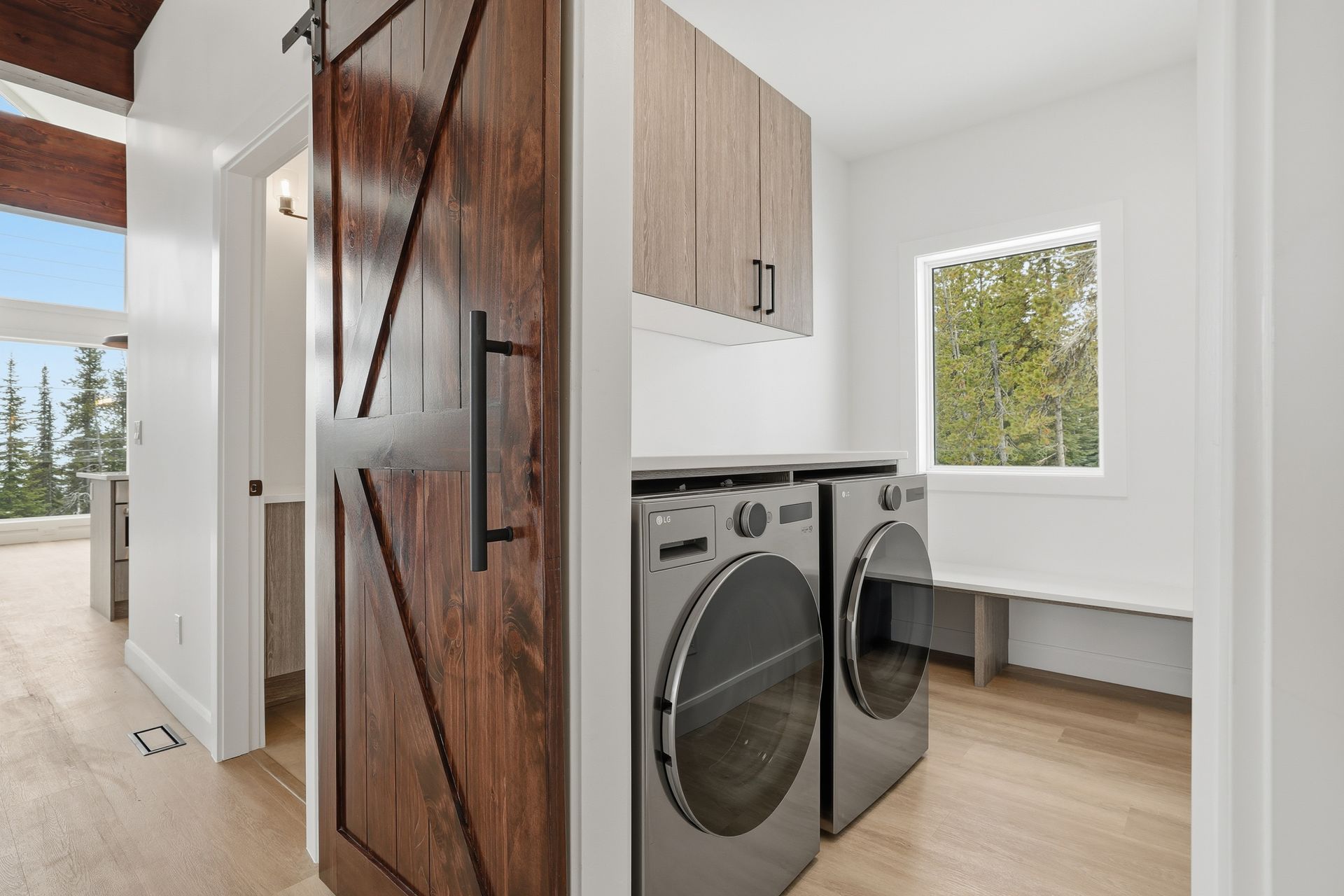 Modern laundry room with stacked washer and dryer, wood cabinetry, and a window view outside