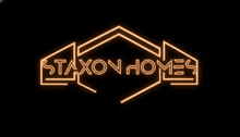 Orange neon “STAXON HOMES” logo on a black background