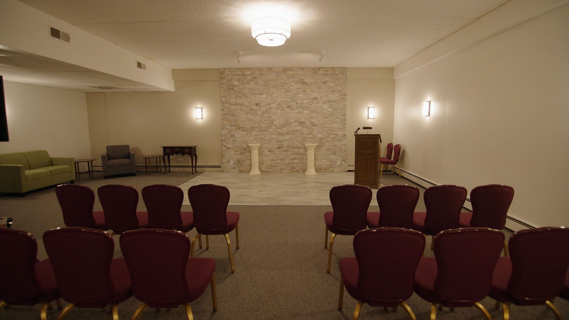 Interior of a chapel with rows of red chairs facing a podium and decorative wall.