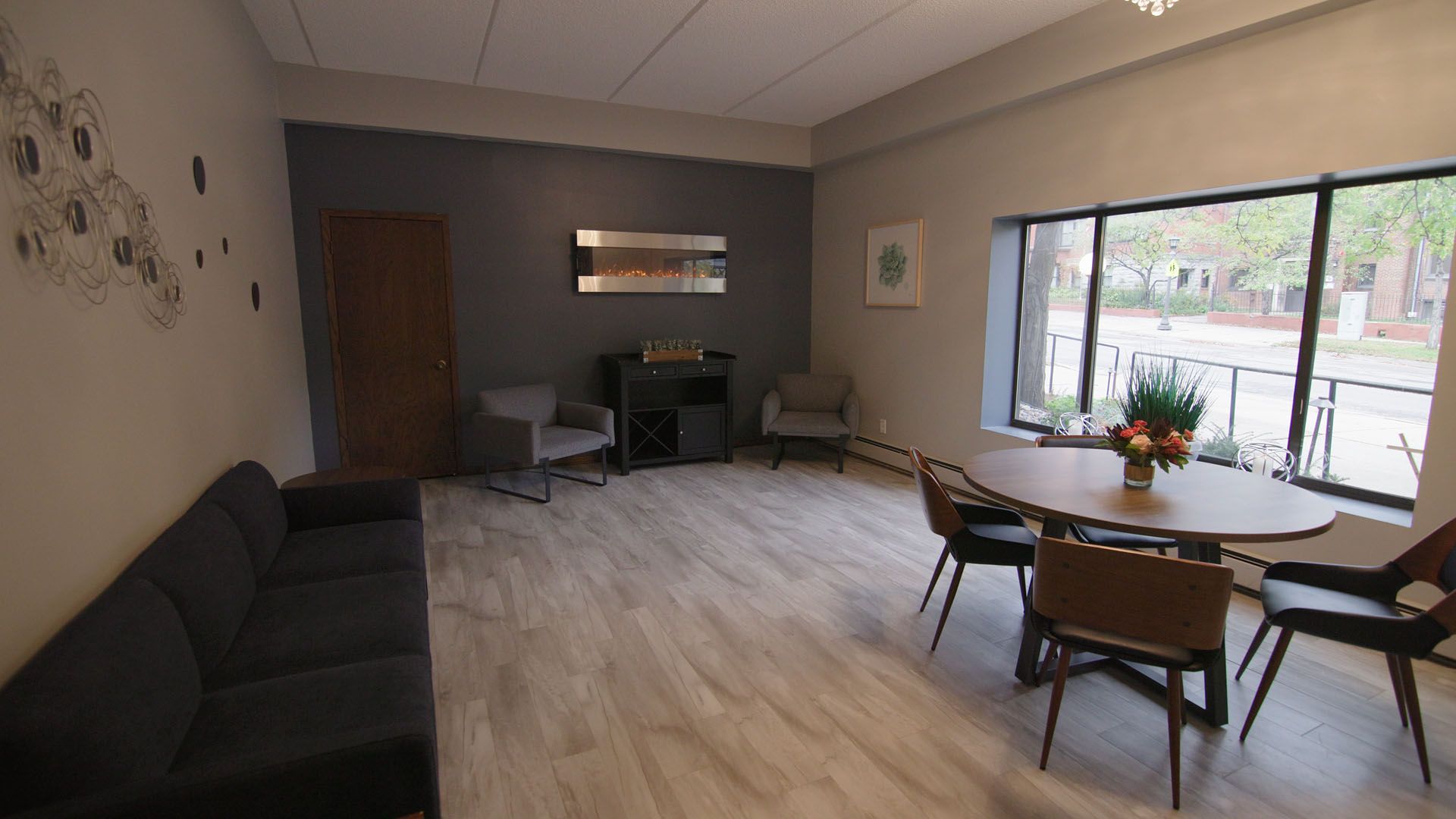 A furnished waiting room with a sofa, chairs, round table by a window, and decorative wall art.